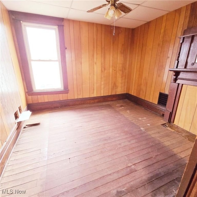 unfurnished room with wooden walls, baseboards, ceiling fan, a drop ceiling, and hardwood / wood-style floors