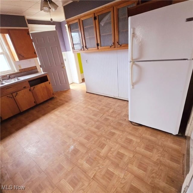 kitchen featuring a sink, glass insert cabinets, brown cabinets, and freestanding refrigerator