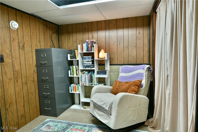 living area featuring a drop ceiling and wood walls