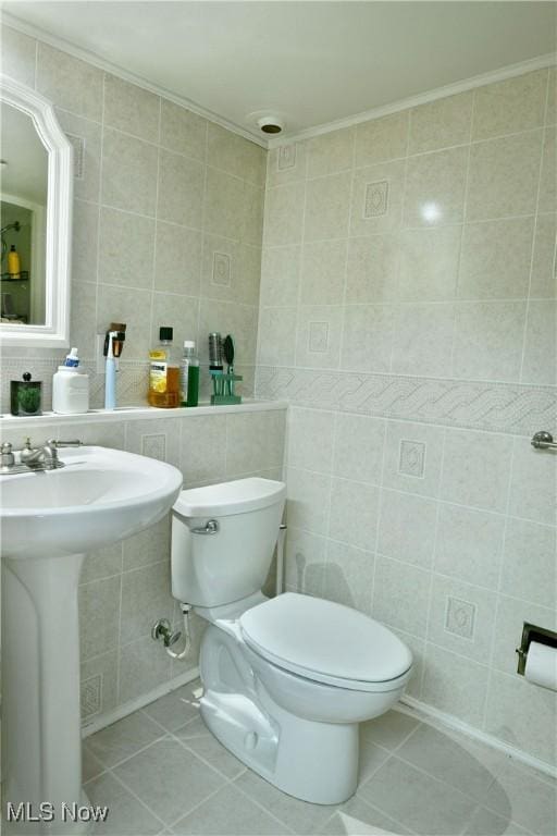 half bathroom with tile patterned flooring, toilet, tile walls, and crown molding