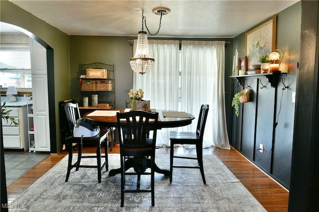 dining room with a notable chandelier, wood finished floors, and arched walkways