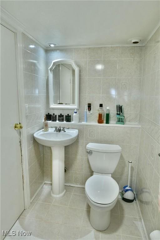 half bathroom with tile patterned floors, toilet, tile walls, and a sink