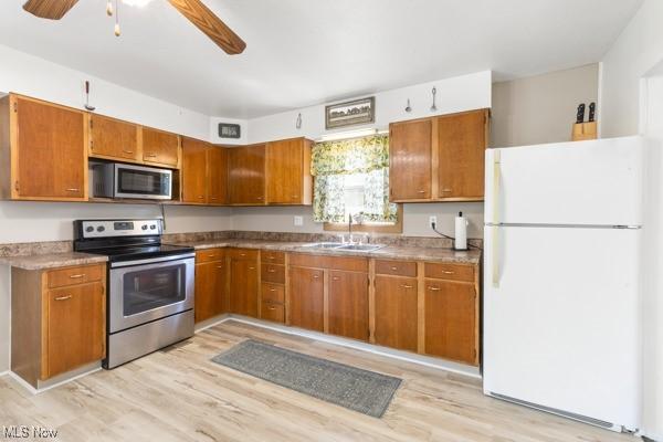 kitchen featuring brown cabinets, a ceiling fan, appliances with stainless steel finishes, and light wood-style flooring