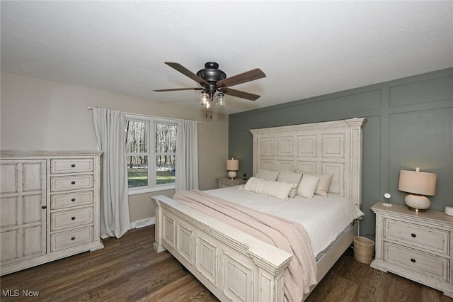 bedroom with ceiling fan, dark wood-style floors, and a decorative wall