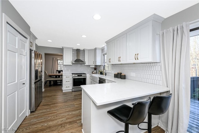 kitchen with backsplash, a wealth of natural light, appliances with stainless steel finishes, a peninsula, and wall chimney exhaust hood