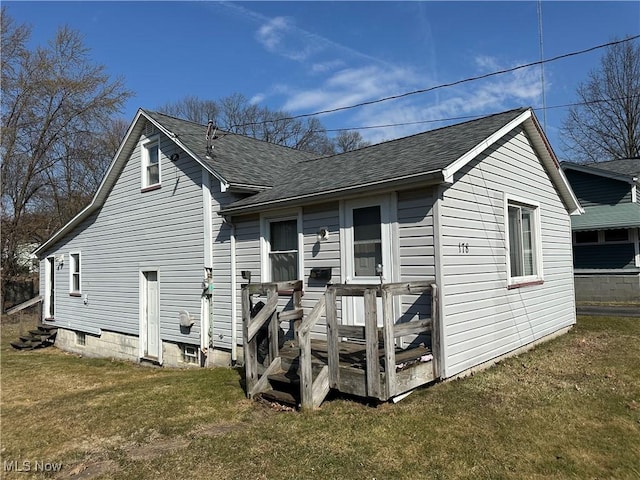 rear view of house with a lawn, entry steps, and roof with shingles