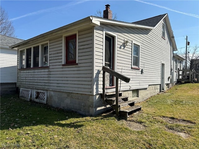 view of front of home with entry steps, a chimney, a front yard, and roof with shingles