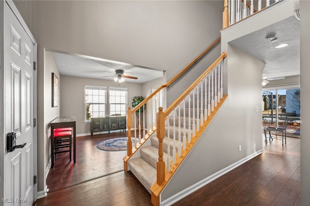 staircase featuring a ceiling fan, baseboards, and hardwood / wood-style flooring