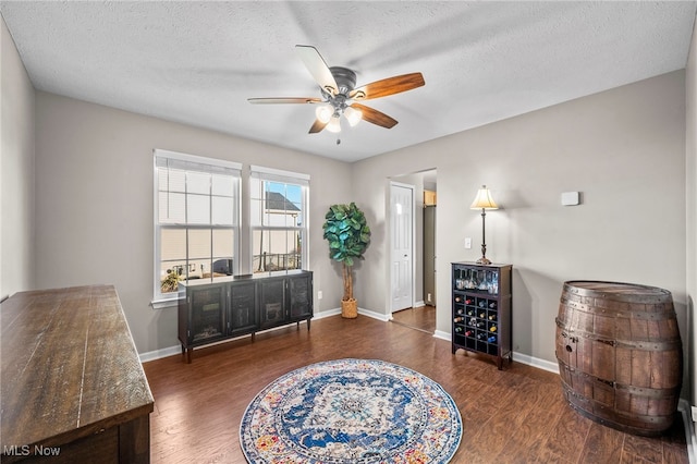 living area with a textured ceiling, wood finished floors, baseboards, and ceiling fan