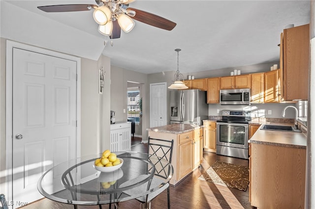 kitchen featuring light brown cabinets, a center island, appliances with stainless steel finishes, hanging light fixtures, and a sink