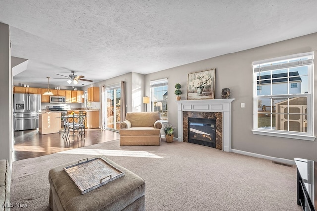 living room featuring a high end fireplace, visible vents, baseboards, a textured ceiling, and dark colored carpet