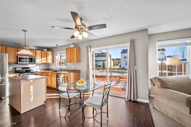 kitchen with dark wood-style floors, a sink, hanging light fixtures, stainless steel appliances, and a center island