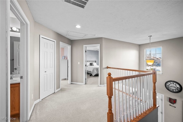 hallway featuring visible vents, baseboards, an upstairs landing, carpet flooring, and a textured ceiling