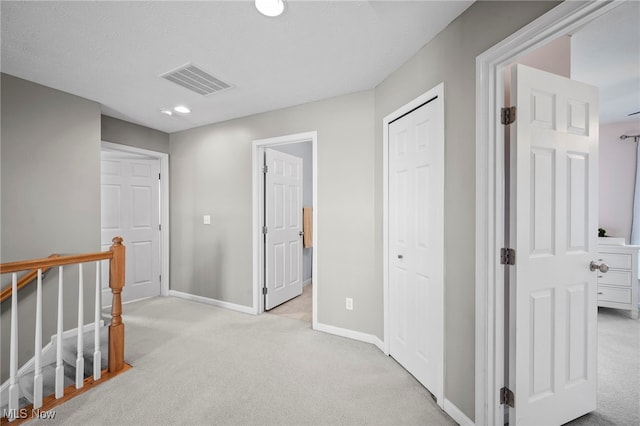 hall with light colored carpet, an upstairs landing, visible vents, and baseboards