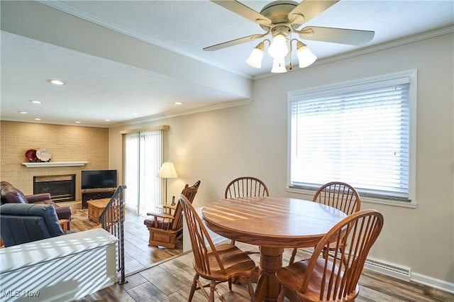 dining room with ceiling fan, baseboards, ornamental molding, a fireplace, and wood finished floors