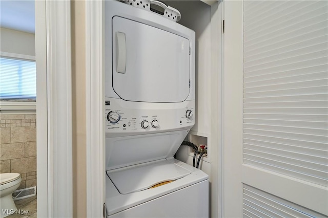 clothes washing area with laundry area, stacked washer / dryer, tile walls, and visible vents