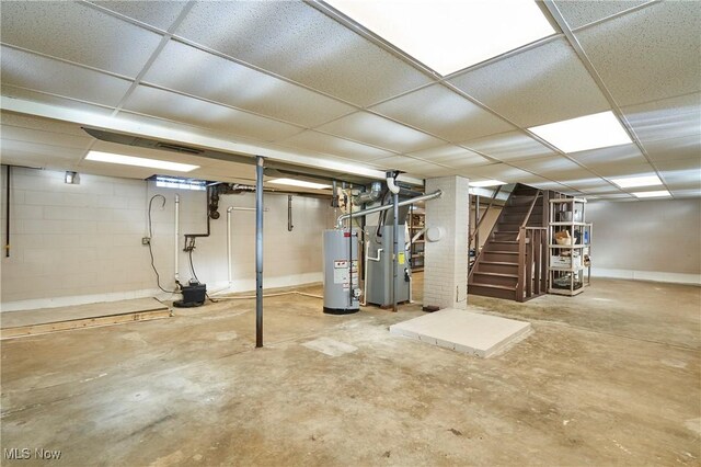 finished basement featuring a paneled ceiling, gas water heater, stairs, heating unit, and concrete block wall