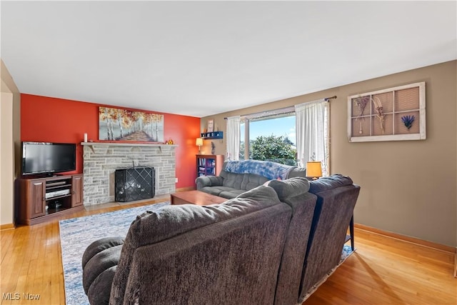 living area with a stone fireplace, wood finished floors, and baseboards