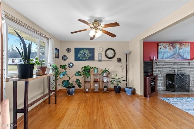 interior space with baseboards, a stone fireplace, a ceiling fan, and hardwood / wood-style flooring