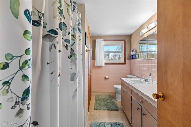 bathroom featuring toilet, vanity, a shower with curtain, tile patterned floors, and tile walls