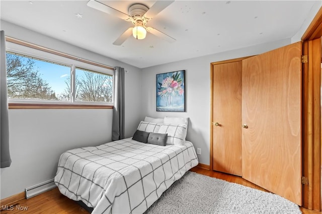 bedroom with a baseboard heating unit, wood finished floors, baseboards, and a ceiling fan