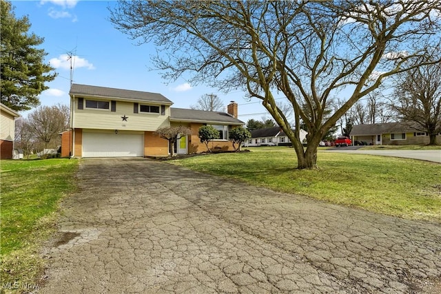 tri-level home with brick siding, a front lawn, aphalt driveway, a chimney, and an attached garage