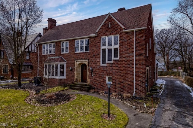 view of front of home featuring a front lawn, brick siding, central AC, and a chimney