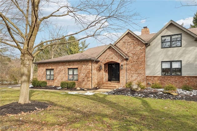 view of front of home with a shingled roof, a front lawn, brick siding, and a chimney