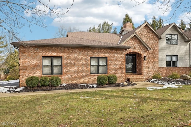 view of front of home with brick siding, a chimney, a front yard, and roof with shingles