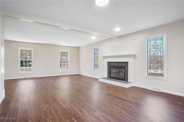 unfurnished living room with visible vents, beamed ceiling, a glass covered fireplace, baseboards, and dark wood-style flooring