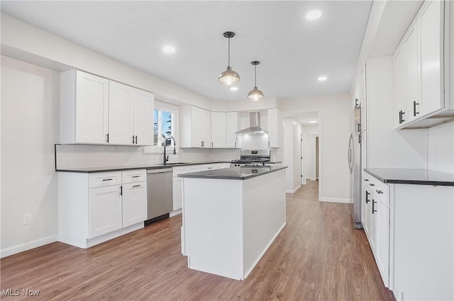 kitchen with dark countertops, wall chimney range hood, light wood-type flooring, and appliances with stainless steel finishes