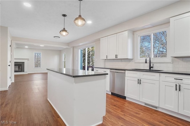 kitchen featuring a sink, stainless steel dishwasher, dark countertops, wood finished floors, and a center island