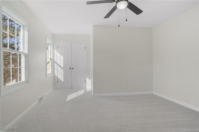 carpeted spare room featuring visible vents, baseboards, a healthy amount of sunlight, and ceiling fan