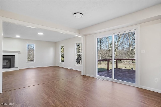 unfurnished living room with baseboards, wood finished floors, a healthy amount of sunlight, and a glass covered fireplace