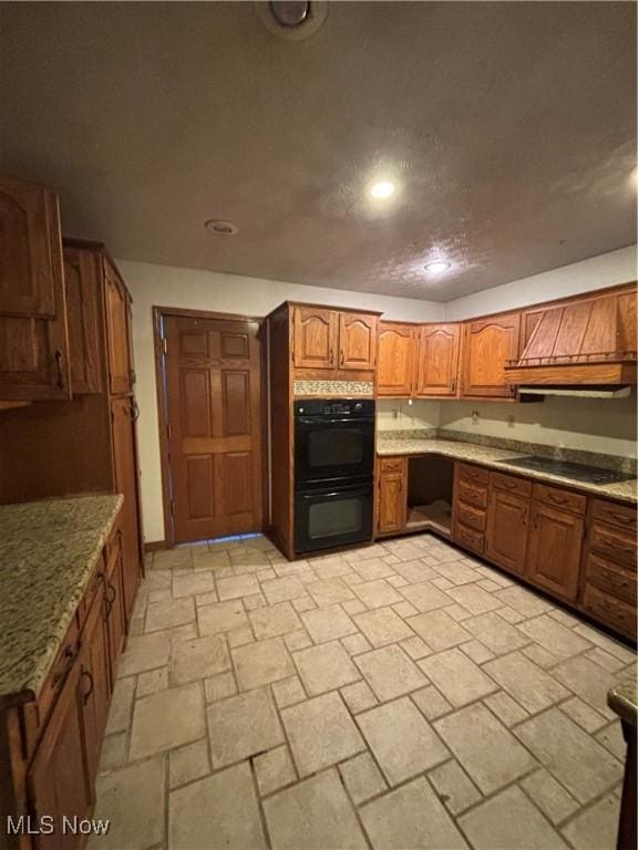 kitchen with brown cabinetry, light stone countertops, built in study area, black appliances, and a textured ceiling