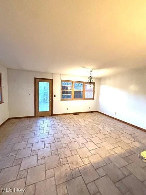 unfurnished room with plenty of natural light, an inviting chandelier, and baseboards