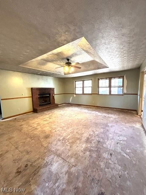 unfurnished living room with a raised ceiling, a fireplace, baseboards, and a textured ceiling