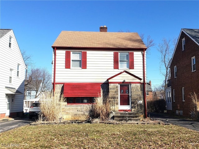 view of front of home featuring stone siding, a front lawn, and a chimney