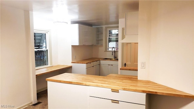 kitchen with butcher block countertops, a sink, open shelves, white cabinetry, and a peninsula