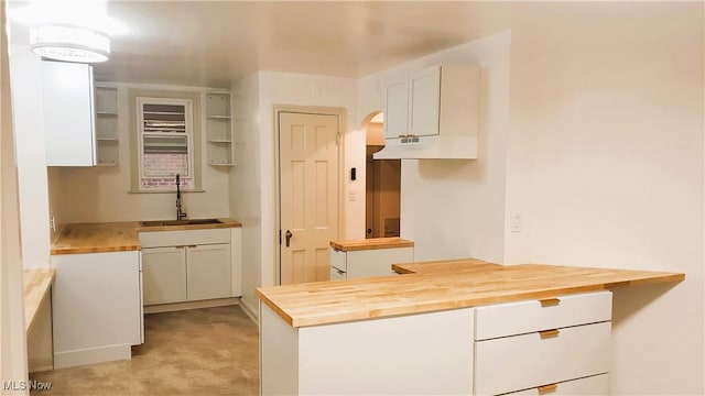 kitchen featuring under cabinet range hood, white cabinets, butcher block counters, and a sink