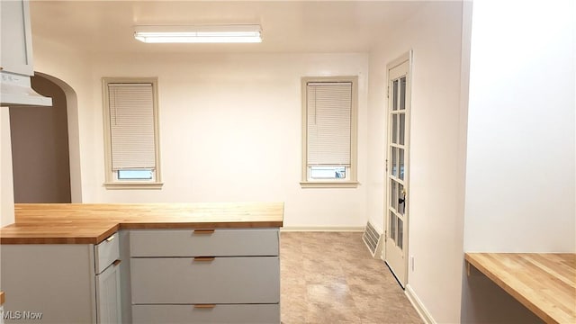 kitchen with visible vents, arched walkways, under cabinet range hood, and wood counters