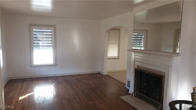 unfurnished living room featuring a fireplace with flush hearth, baseboards, and wood finished floors