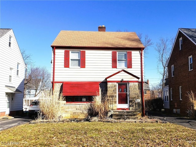 view of front facade featuring stone siding, a chimney, and a front lawn