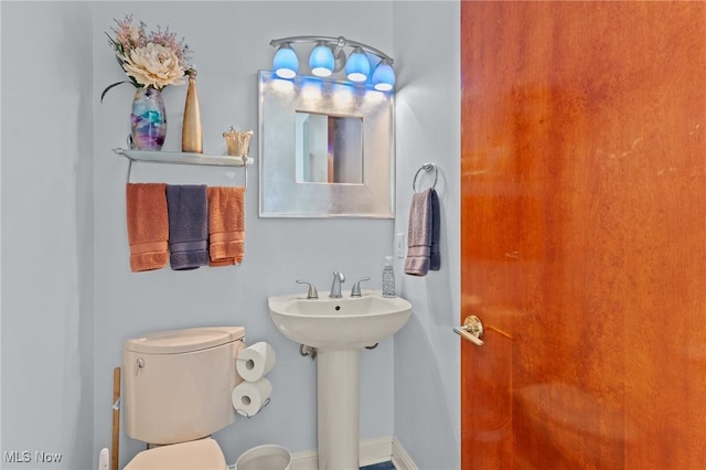 half bath featuring toilet, baseboards, and a sink