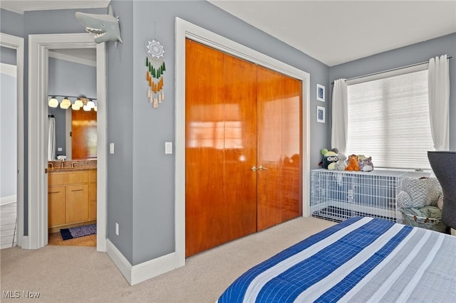 carpeted bedroom featuring ensuite bath, baseboards, and a sink