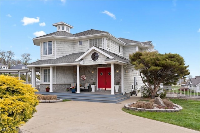 view of front of property featuring stone siding, a porch, and fence