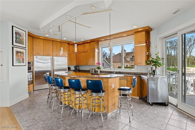 kitchen with dark stone countertops, visible vents, a kitchen island, stainless steel built in fridge, and a kitchen breakfast bar