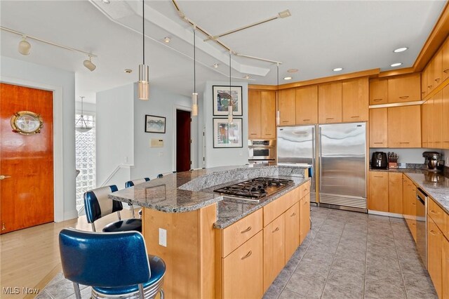 kitchen featuring a kitchen bar, decorative light fixtures, a center island, dark stone counters, and appliances with stainless steel finishes
