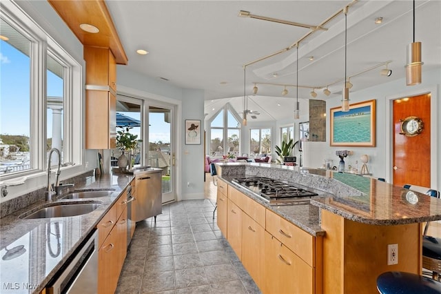 kitchen with a kitchen island, dark stone counters, stainless steel appliances, a sink, and open floor plan