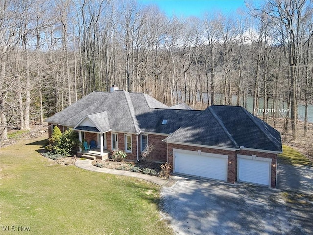 view of front facade featuring aphalt driveway, a wooded view, a front yard, a garage, and brick siding